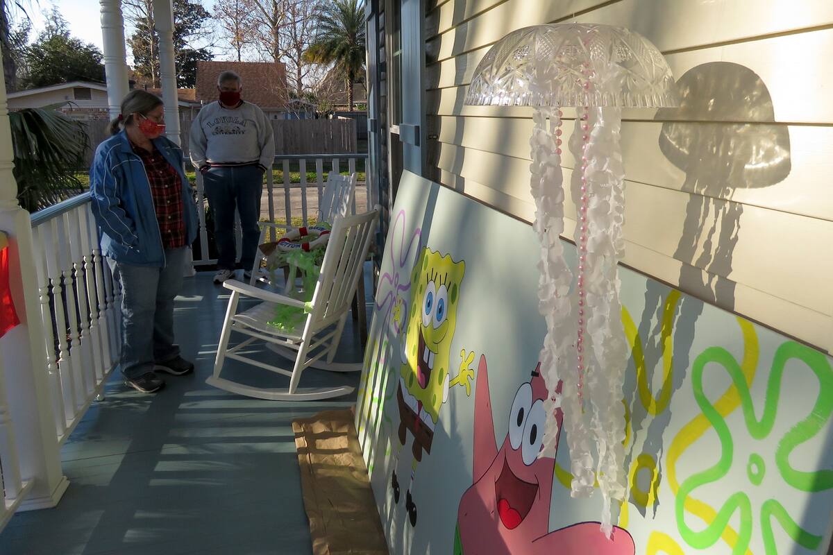 Madeline Fox y su esposo, Tom Fox, parados junto a las decoraciones que hicieron y colocaron en su casa en River Ridge, a las afueras de Nueva Orleans, el miércoles 13 de enero de 2021. Con la cancelación de los tradicionales desfiles de Mardi Gras debido a la pandemia de coronavirus, miles alrededor de la ciudad han decorado sus casas para celebrar el Carnaval. (AP Foto/Janet McConnaughey)