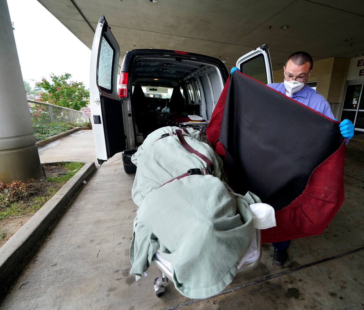 En esta imagen del 18 de agosto de 2021, el empleado de una funeraria local cubre el cuerpo de un paciente de COVID-19 que perdió la vida, mientras lo prepara para trasladarlo a la zona de carga, en el Centro Médico Willis-Knighton de Shreveport, Luisiana. (AP Foto/Gerald Herbert, Archivo)