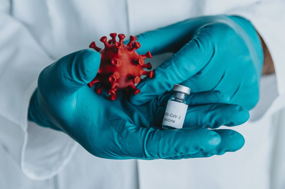 Scientist’s hands holding a SARS-CoV-2 vaccine and coronavirus model in laboratory, NRW, Germany