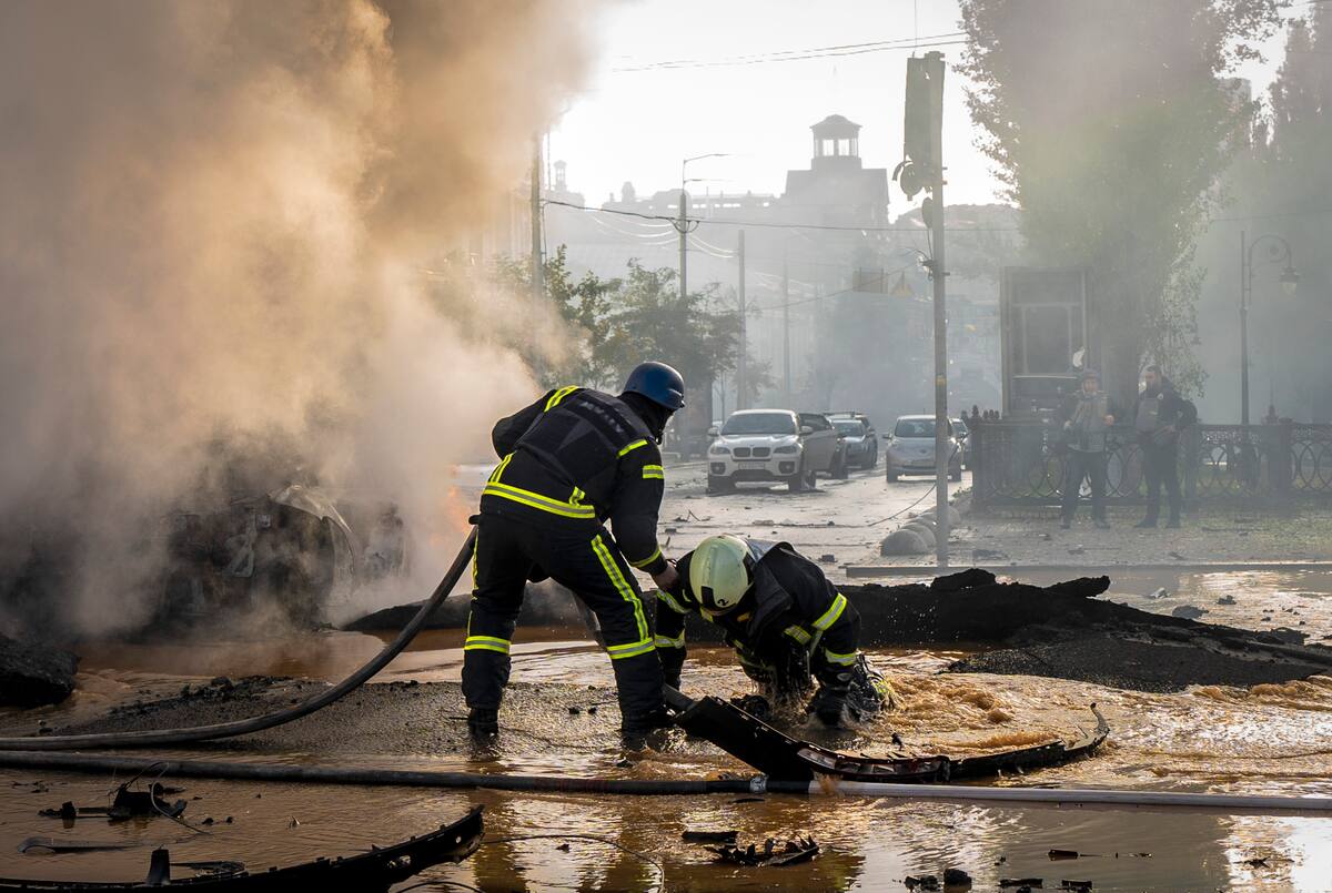 Un bombero ayuda a su compañero a salir de un cráter mientras sofocan las llamas de un auto después de un ataque ruso a Kiev, Ucrania, 10 de octubre de 2022. (AP Foto/Roman Hrytsyna)