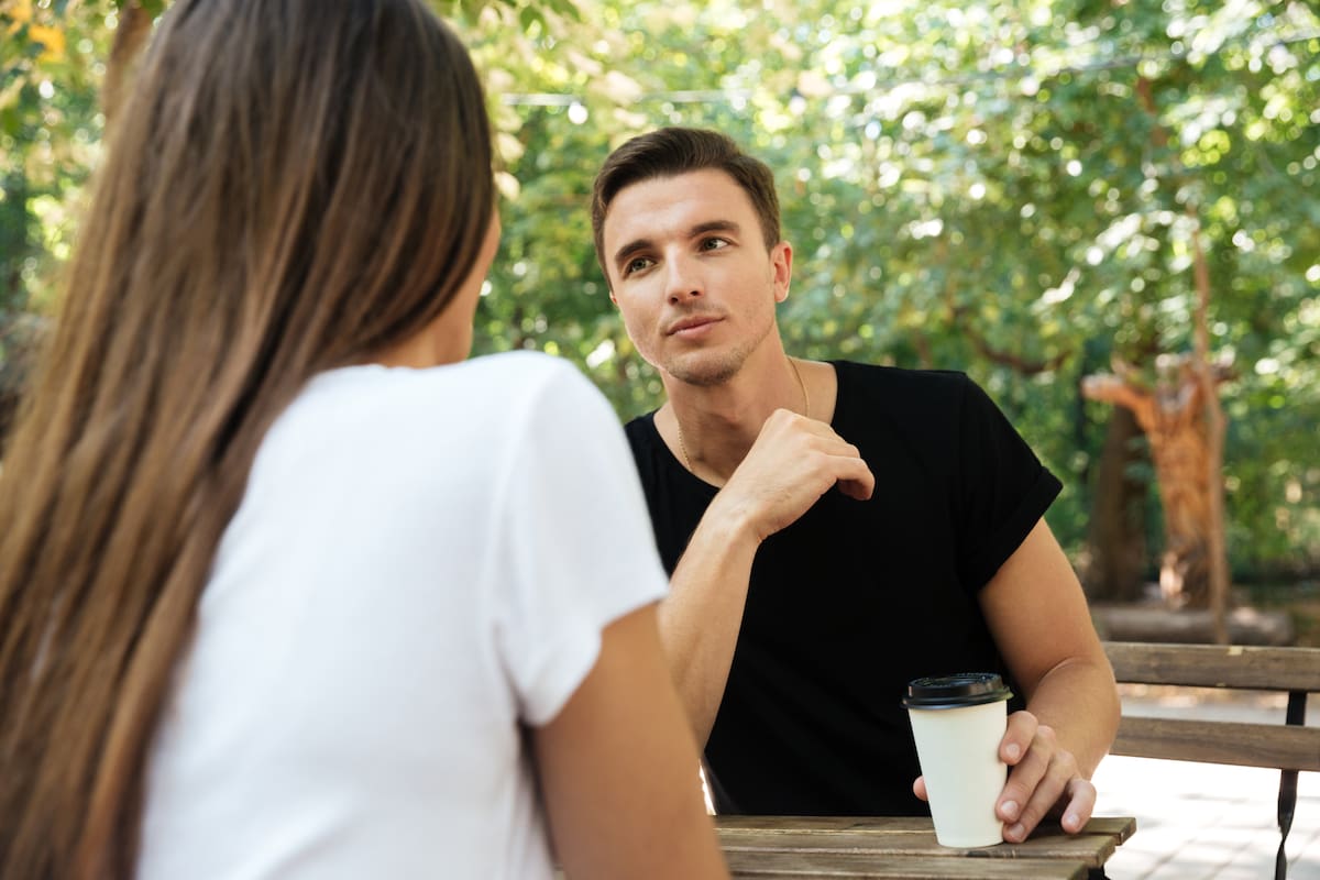 Young bored man sitting and drinking coffee with his girlfriend at a cafe outdoors