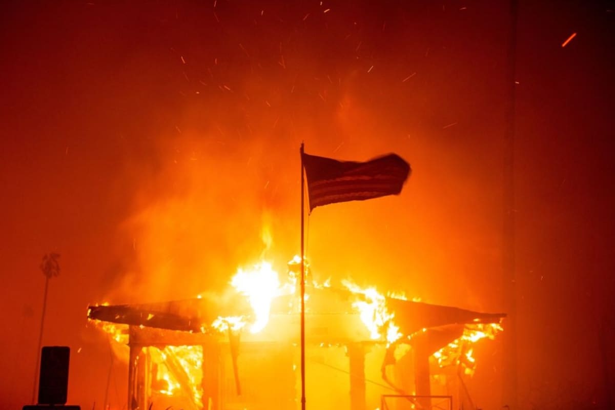 Una bandera estadounidense ondea frente a una estructura envuelta en llamas debido al incendio de Palisades. | Crédito: REUTERS