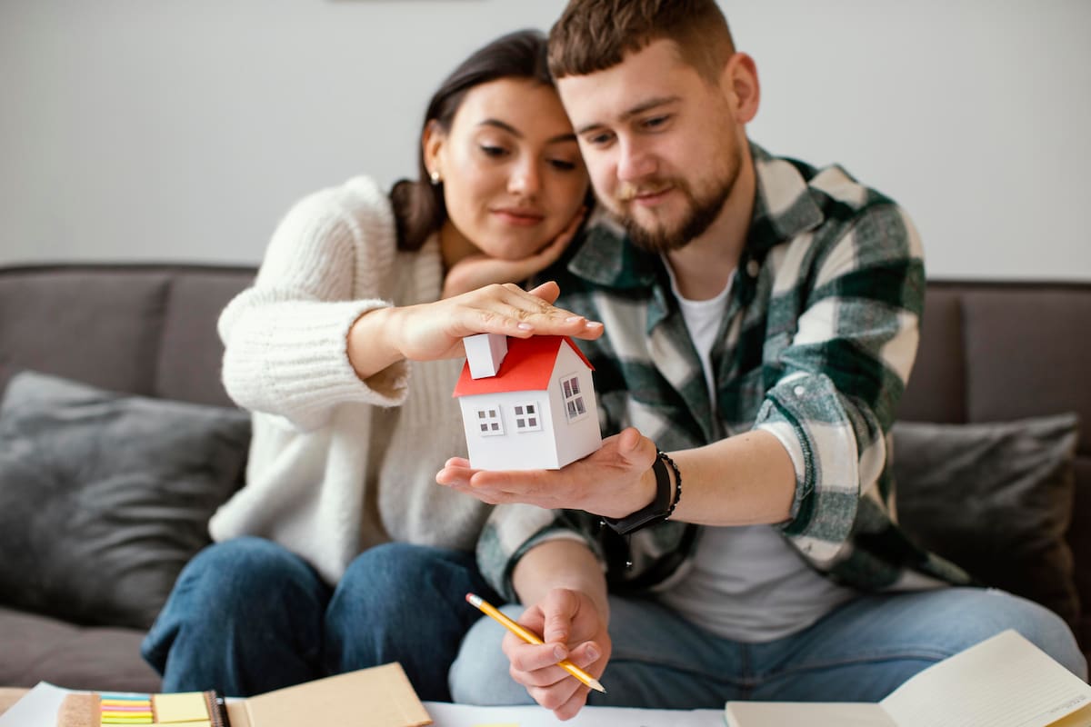 Una pareja sostiene una maqueta de casa mientras revisa documentos sobre la protección del patrimonio familiar mediante un seguro residencial. | Magnific
