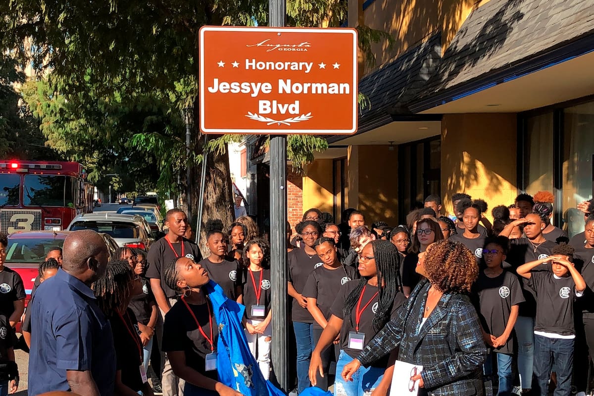 Estudiantes de la Jessye Norman School of the Arts develan un cartel en la calle frente a la escuela en honor de la difunta gran cantante lírica, 11 de octubre de 2019 en Augusta, Georgia. El funeral de la soprano, que murió el 30 de septiembre a los 74 años, se realizó el sábado 12 de octubre de 2'19 en Augusta, su ciudad natal. (AP Foto/Jeffrey Collins)