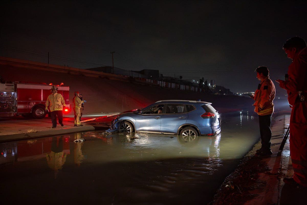 Bomberos utilizaron escaleras para rescatar a los ocupantes del automóvil que terminó dentro de las aguas negras de la canalización. Foto: Border Zoom