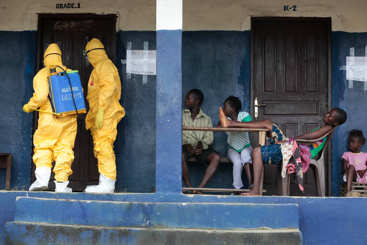 FILE - In this Tuesday, Sept. 30, 2014 file photo, residents of the village of Freeman Reserve, about 30 miles north of Monrovia, in Liberia, watch members of District 13 ambulance service disinfect a room as they pick up six suspected Ebola sufferers that had been quarantined. In a delay that some say may have cost lives, the World Health Organization resisted calling the Ebola outbreak in West Africa a public health emergency until the summer of 2014, two months after staff raised the possibility and long after a senior manager called for a drastic change in strategy, The Associated Press has learned. (AP Photo/Jerome Delay, File)