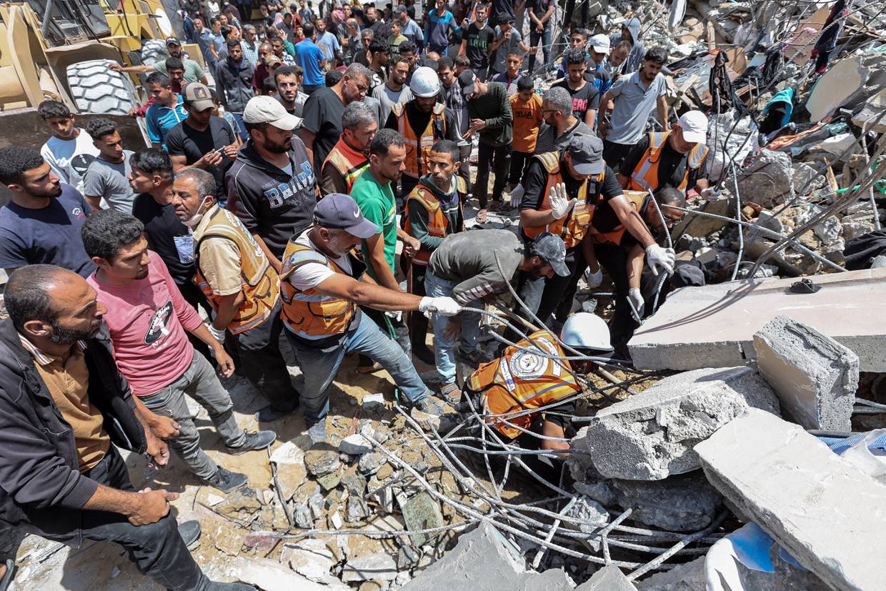 Personas y rescatistas trabajan para recuperar el cuerpo sin vida de un palestino atrapado bajo los escombros de una casa alcanzada por un ataque israelí, en medio del actual conflicto entre Israel y el grupo islamista palestino Hamás, en el campo de refugiados de Nuseirat, en el centro de la Franja de Gaza, 14 de mayo de 2024. REUTERS/Ramadan Abed