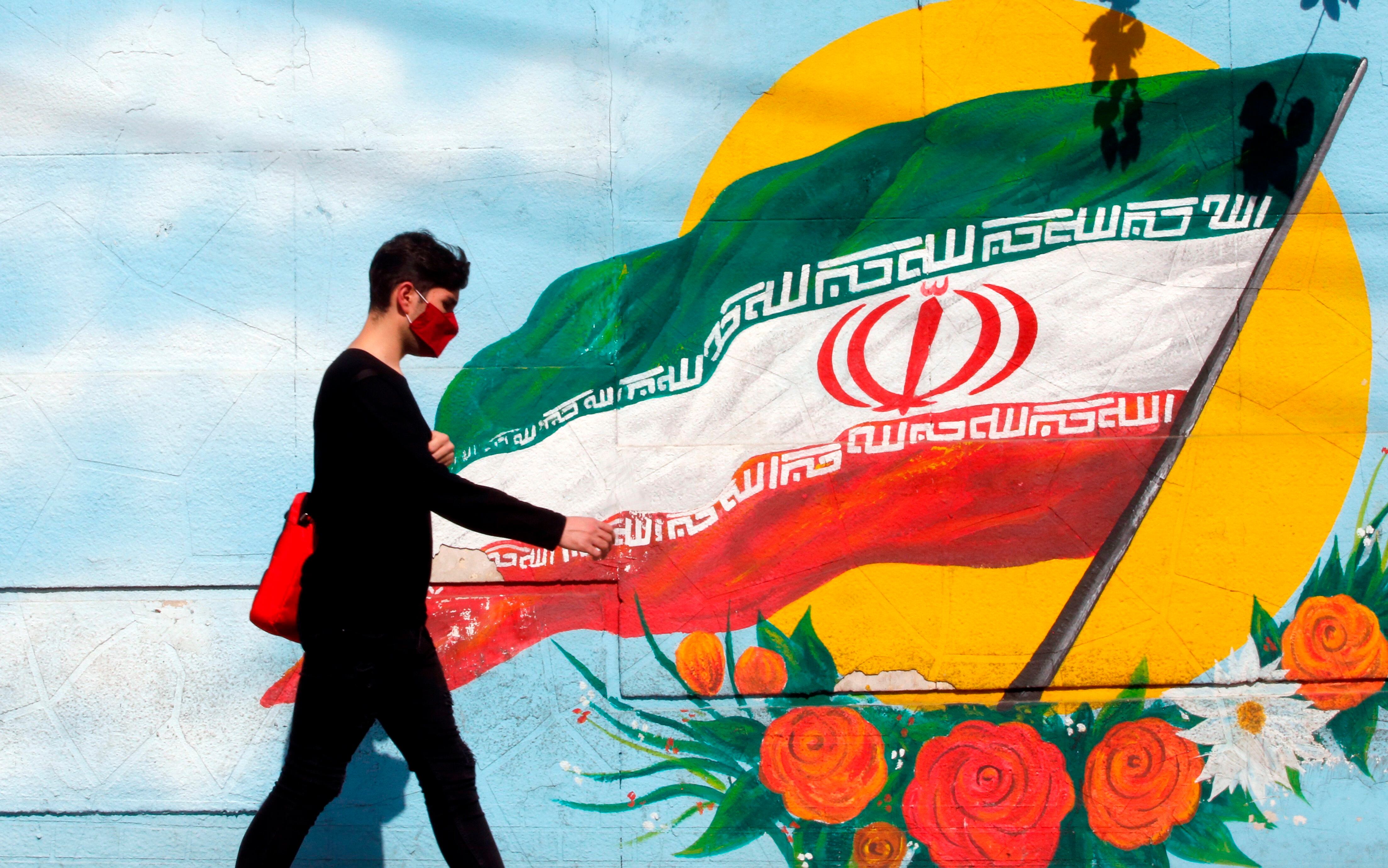 -FOTODELDÍA- TEHERÁN (IRÁN), 17/06/2021.- Un joven camina frente a un mural pintado con la bandera nacional iraní, este jueves en Teherán (Irán). Más de 59 millones de iraníes están llamados mañana a las urnas para elegir un nuevo presidente, en unos comicios marcados por una presencia mayoritaria de candidatos conservadores y en los que está en juego la participación. EFE/ Abedin Taherkenareh
